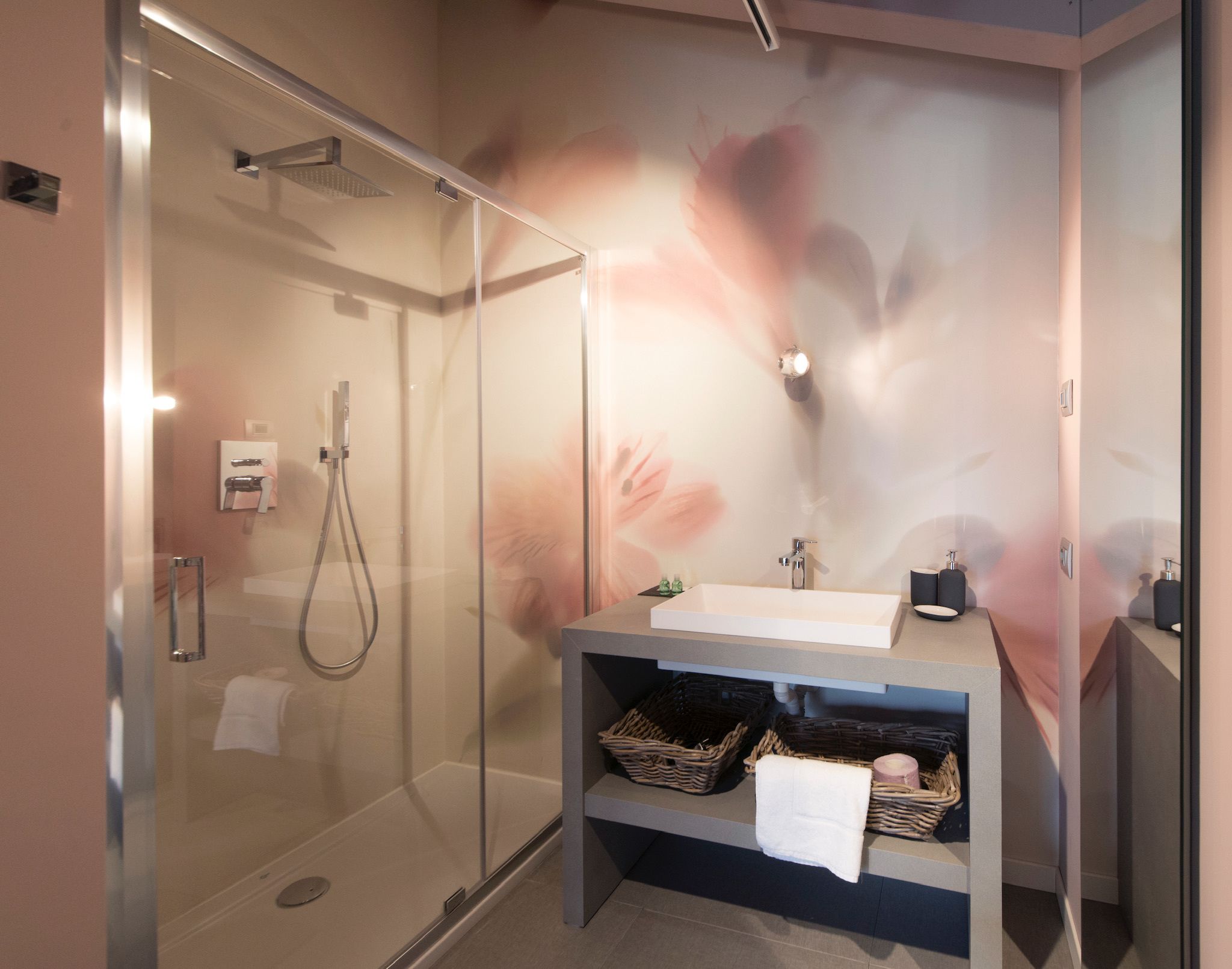 Un baño moderno con cabina de ducha de vidrio, tocador con lavabo y espejo, y dispensador de jabón de pared.