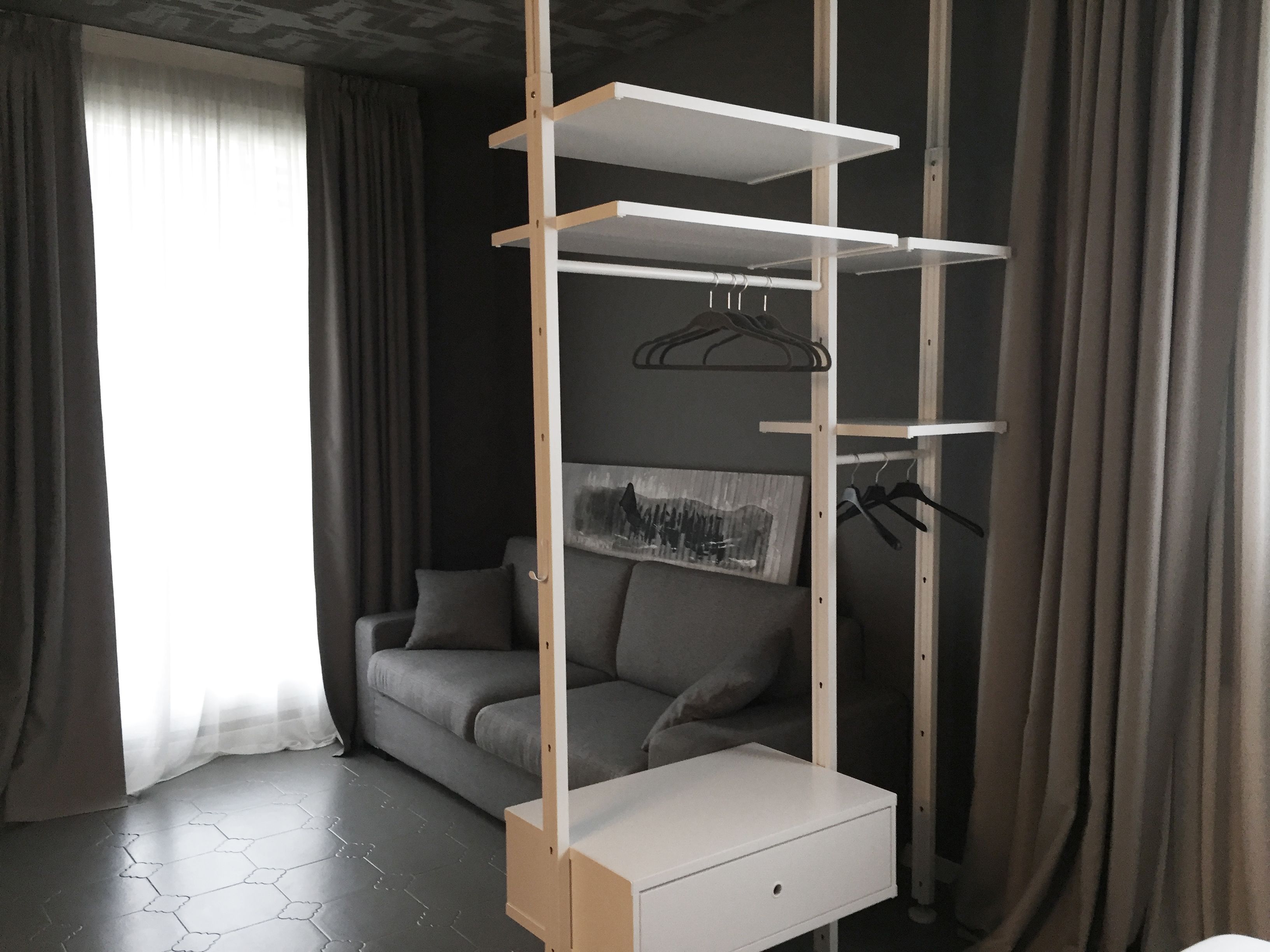 Une pièce moderne avec un canapé gris, un meuble de rangement blanc suspendu et un tableau au mur.