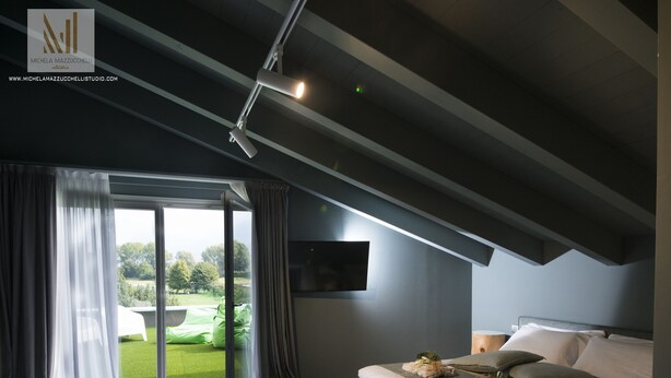 A modern bedroom with a bed, a TV, and a view of a green lawn through a sliding door. - Art B&B Design (Costa Volpino)