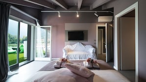 A modern bedroom with a large bed, a TV mounted on the wall, and a sliding glass door leading to a balcony. - Art B&B Design (Costa Volpino)