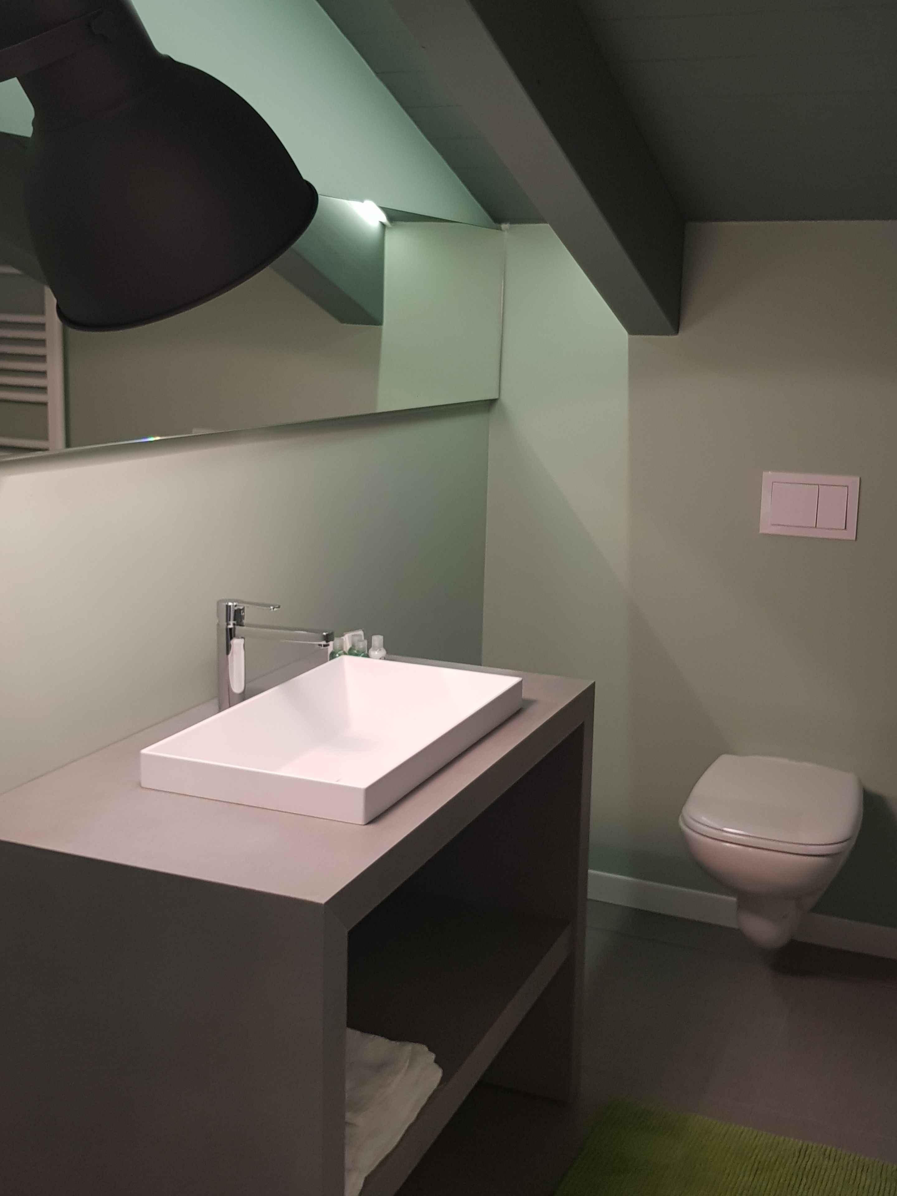 A modern bathroom with a white sink, a mirror, a toilet, and a green accent wall.