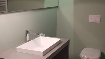 A modern bathroom with a white sink, a mirror, a toilet, and a green accent wall.