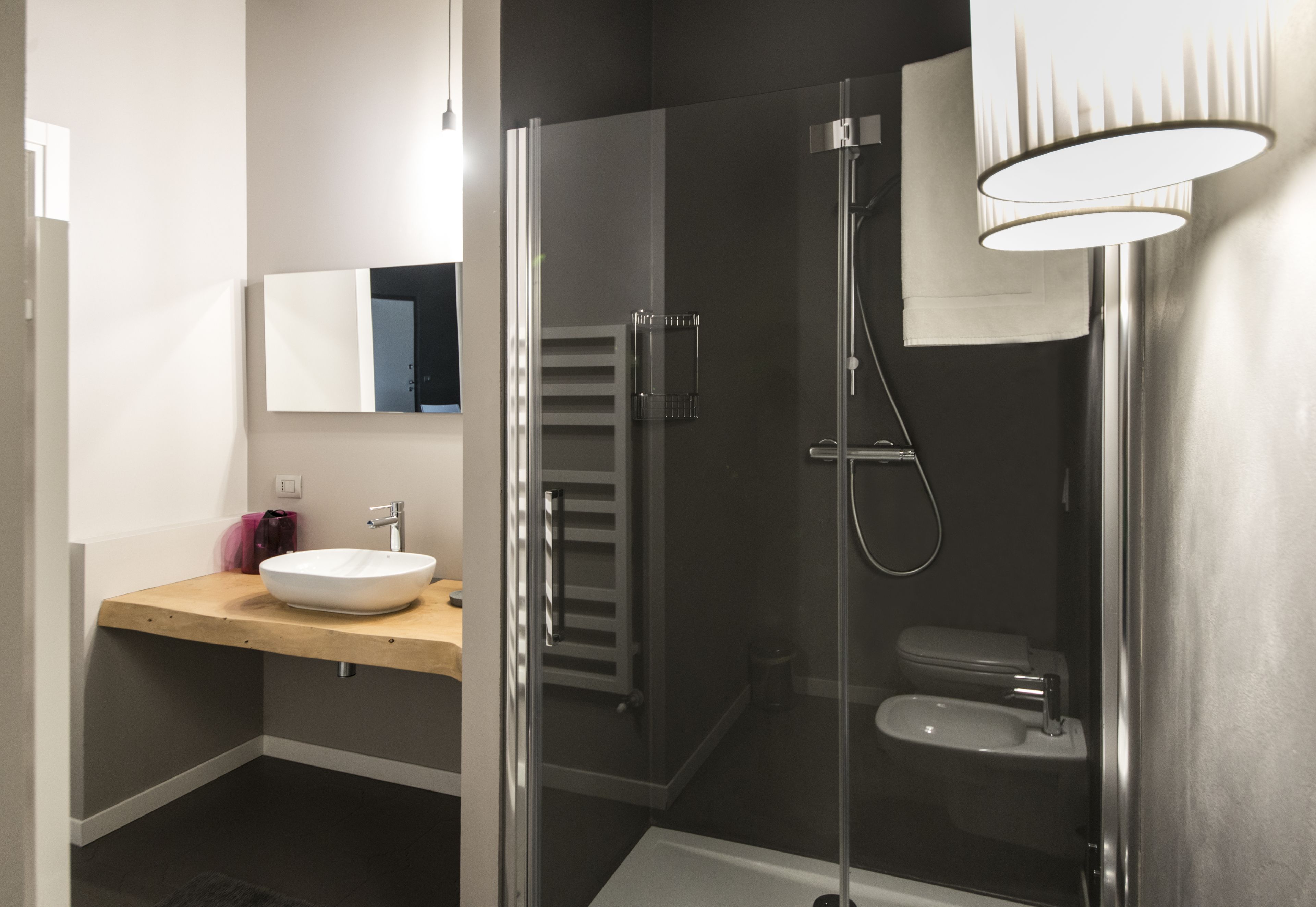 Een moderne badkamer met een douchecabine van glas, een houten wastafelmeubel en een witte wasbak.
