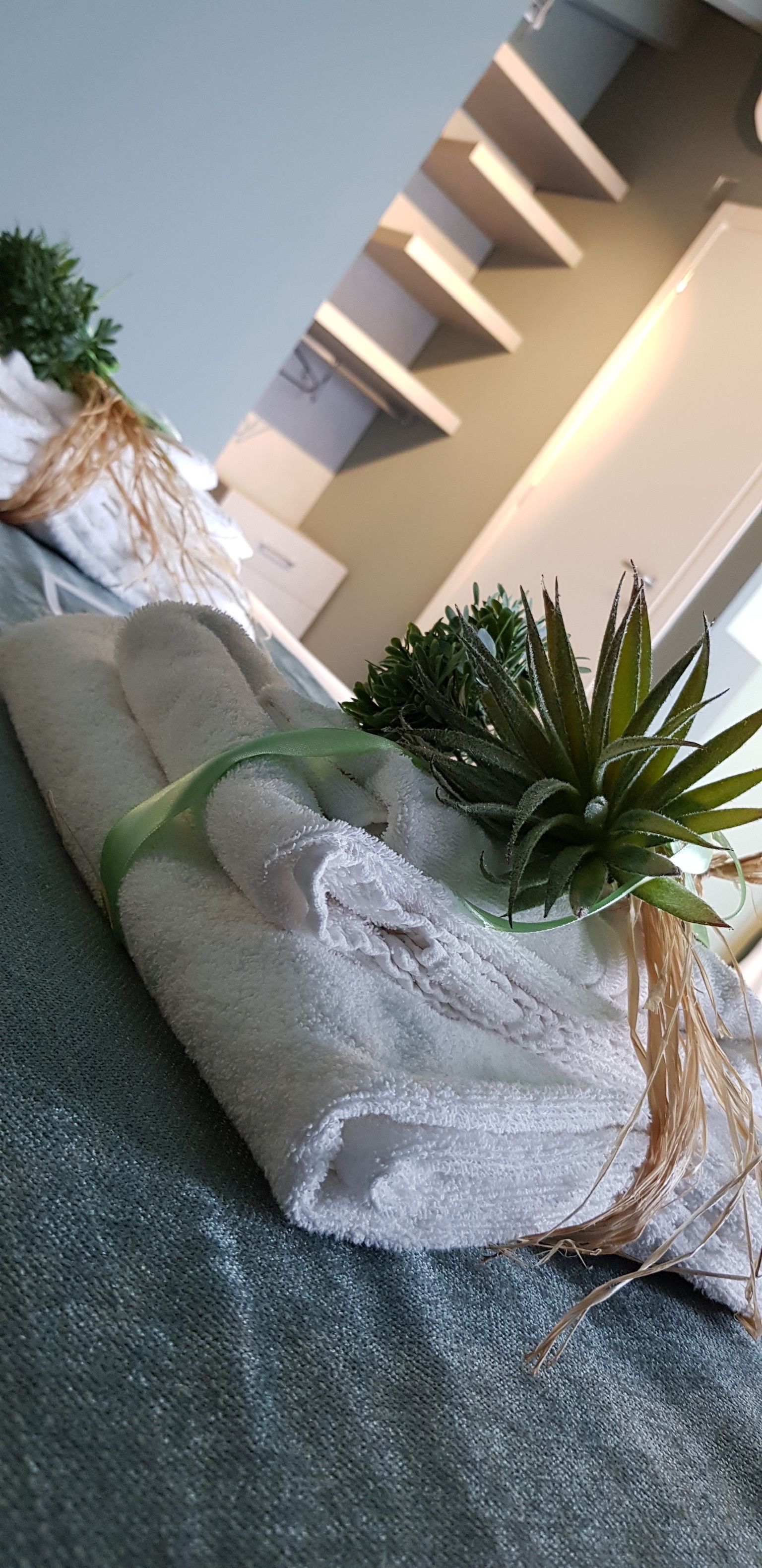 A neatly folded white towel with a green ribbon, placed on a textured fabric surface.