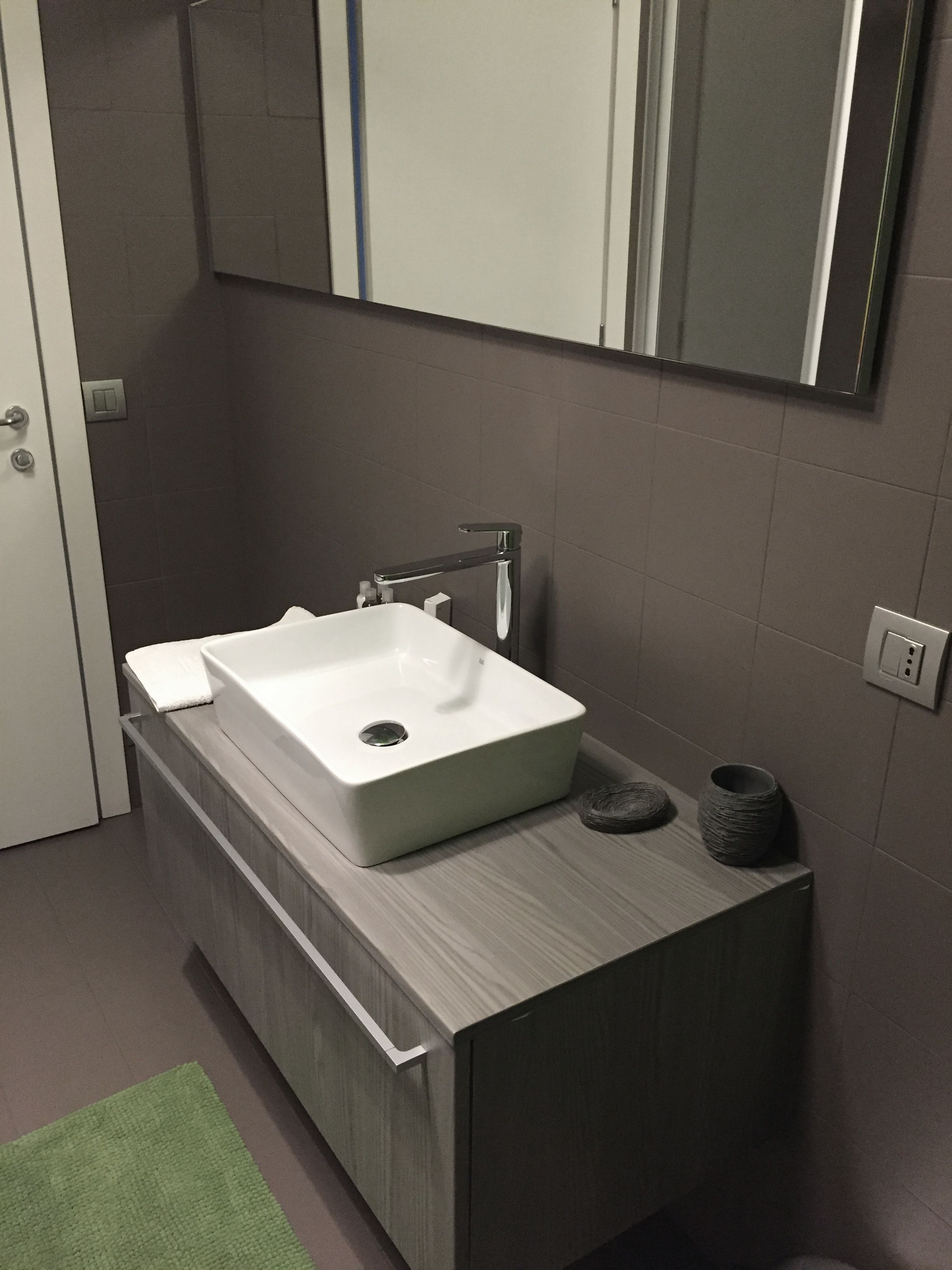 Un baño moderno con un lavamanos blanco, un espejo encima y una alfombra verde en el suelo.