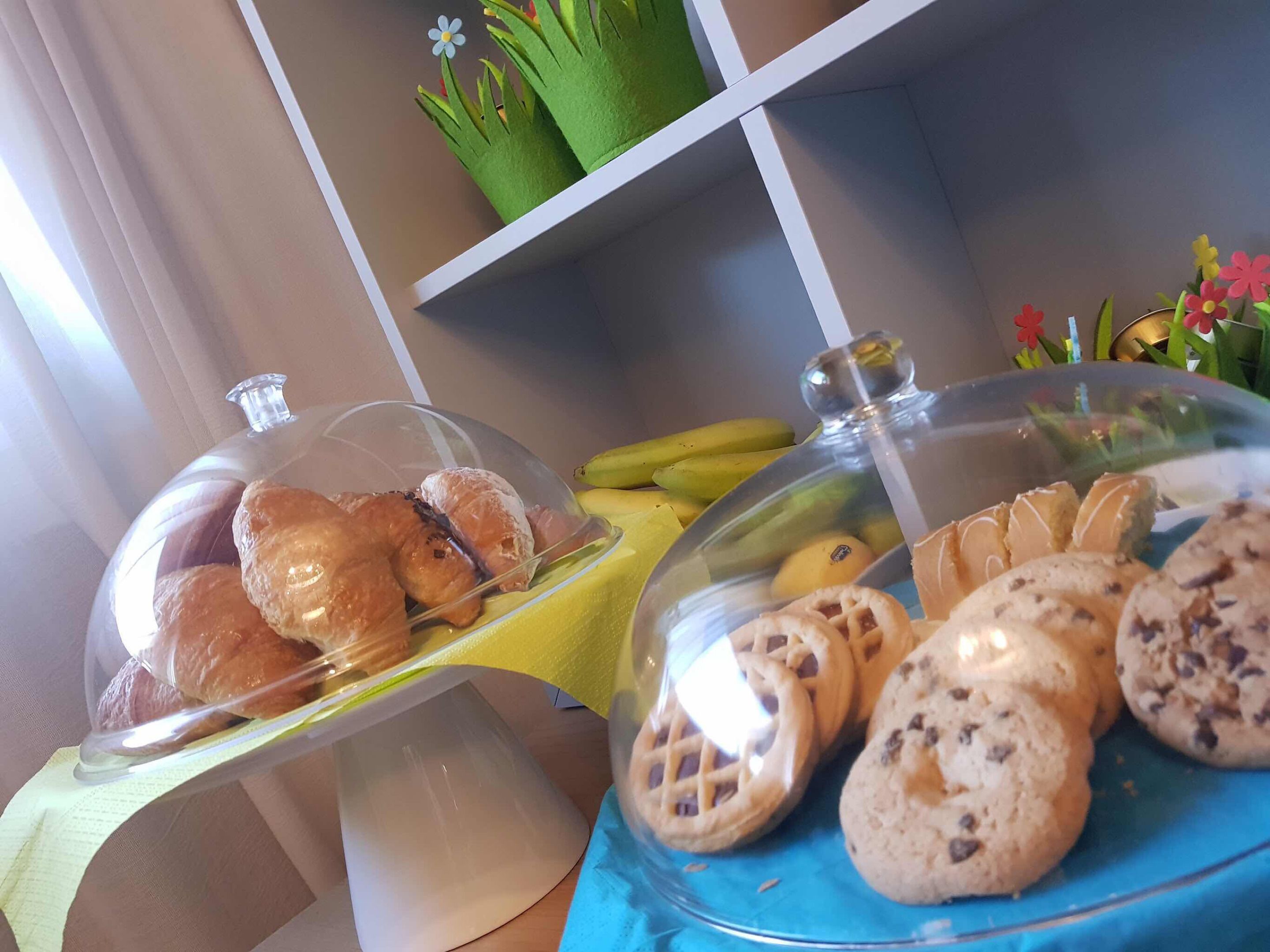 A buffet setup with covered food displays, including pastries and cookies, and a yellow tablecloth.