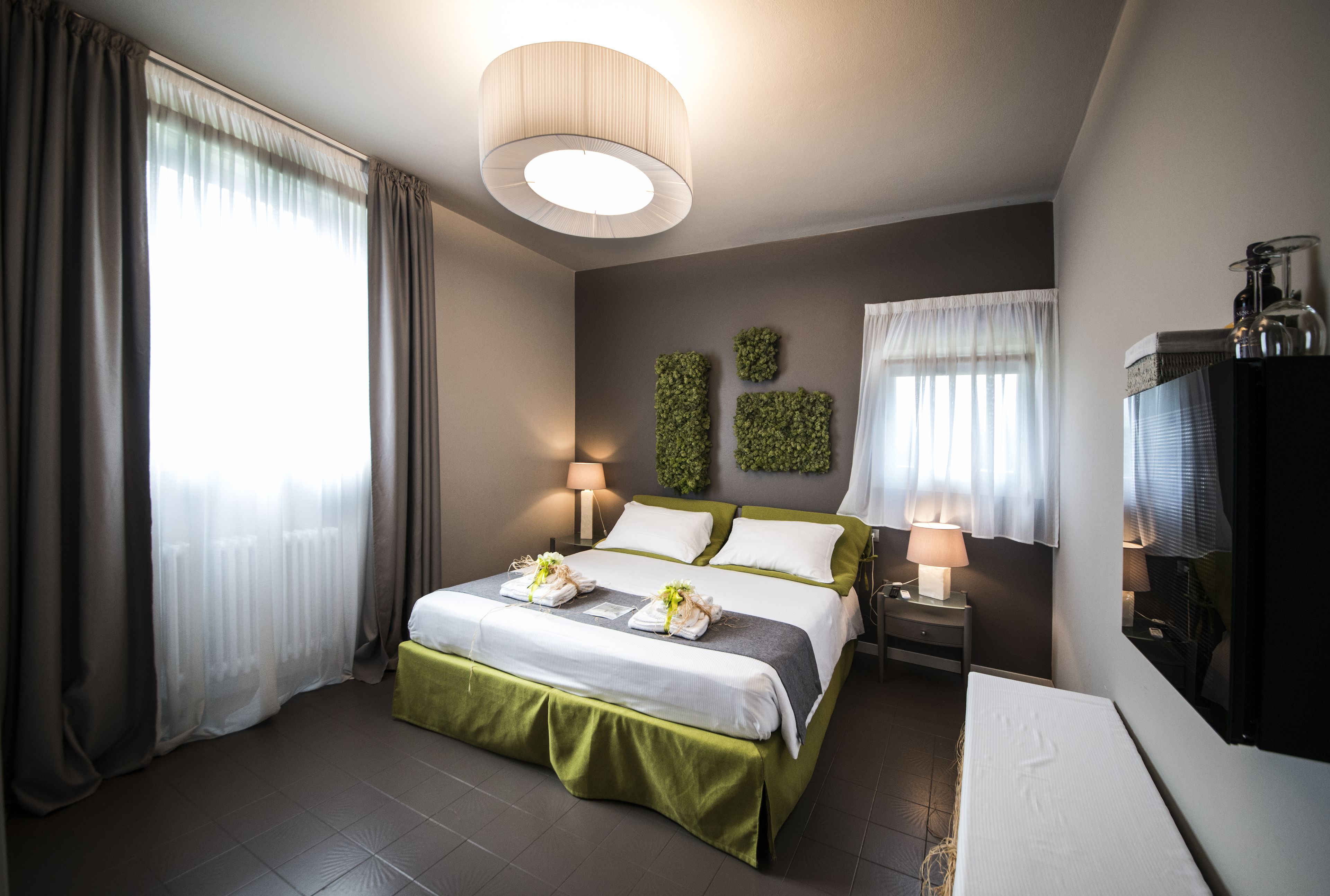 Habitación de hotel moderna con una cama grande, una mesita de noche con lámpara, televisión y vistas al exterior.