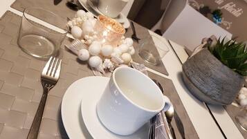 A neatly arranged dining table with a white cup, saucer, and glass, a fork, a knife, and a napkin. There is a small potted plant and decorative white spheres on the table.