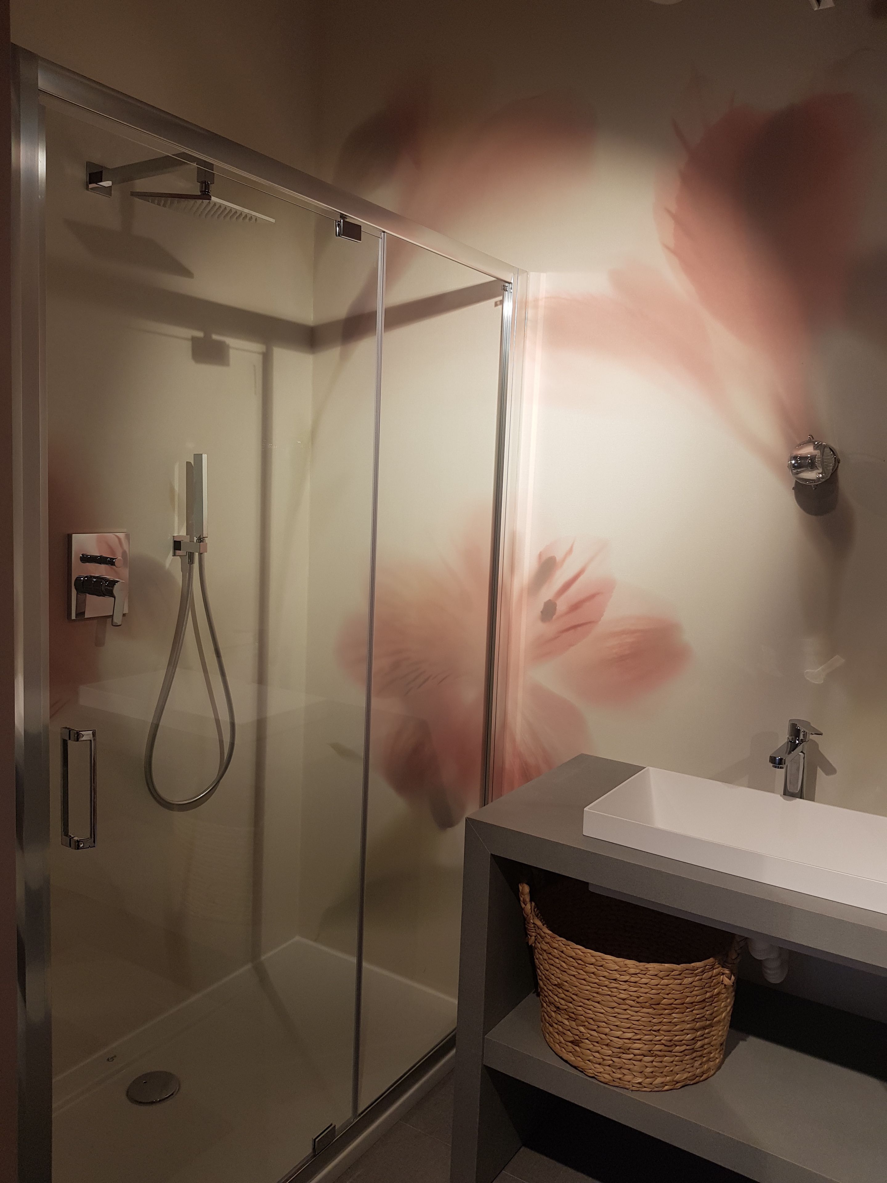 Une salle de bain moderne avec une douche à parois de verre, un lavabo blanc et un panier en osier posé sur l’étagère.