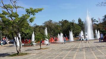 A public square with fountains, trees, and people.