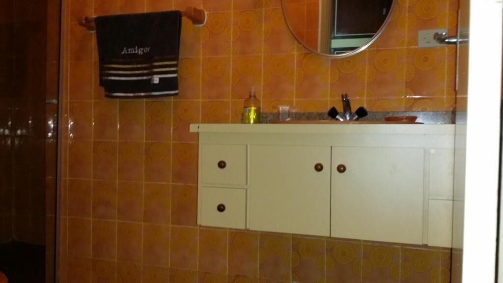 Casa de banho com toucador branco, um porta-toalhas com uma toalha com a etiqueta "Amigo" e um espelho sobre a pia.