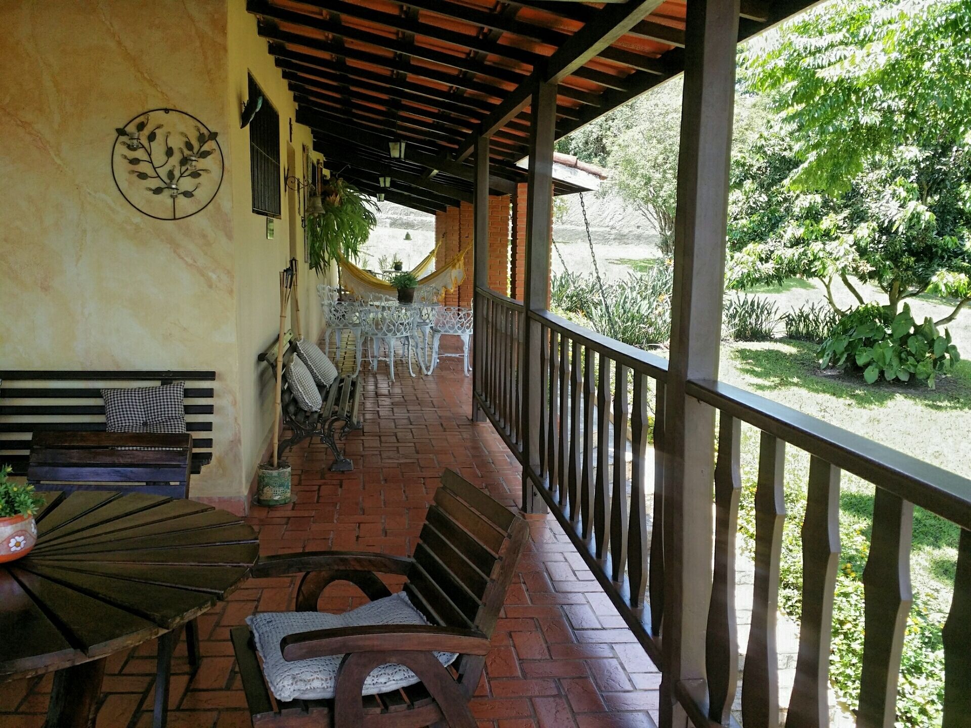 A covered outdoor seating area with a brick floor, metal railings, and a view of a garden.