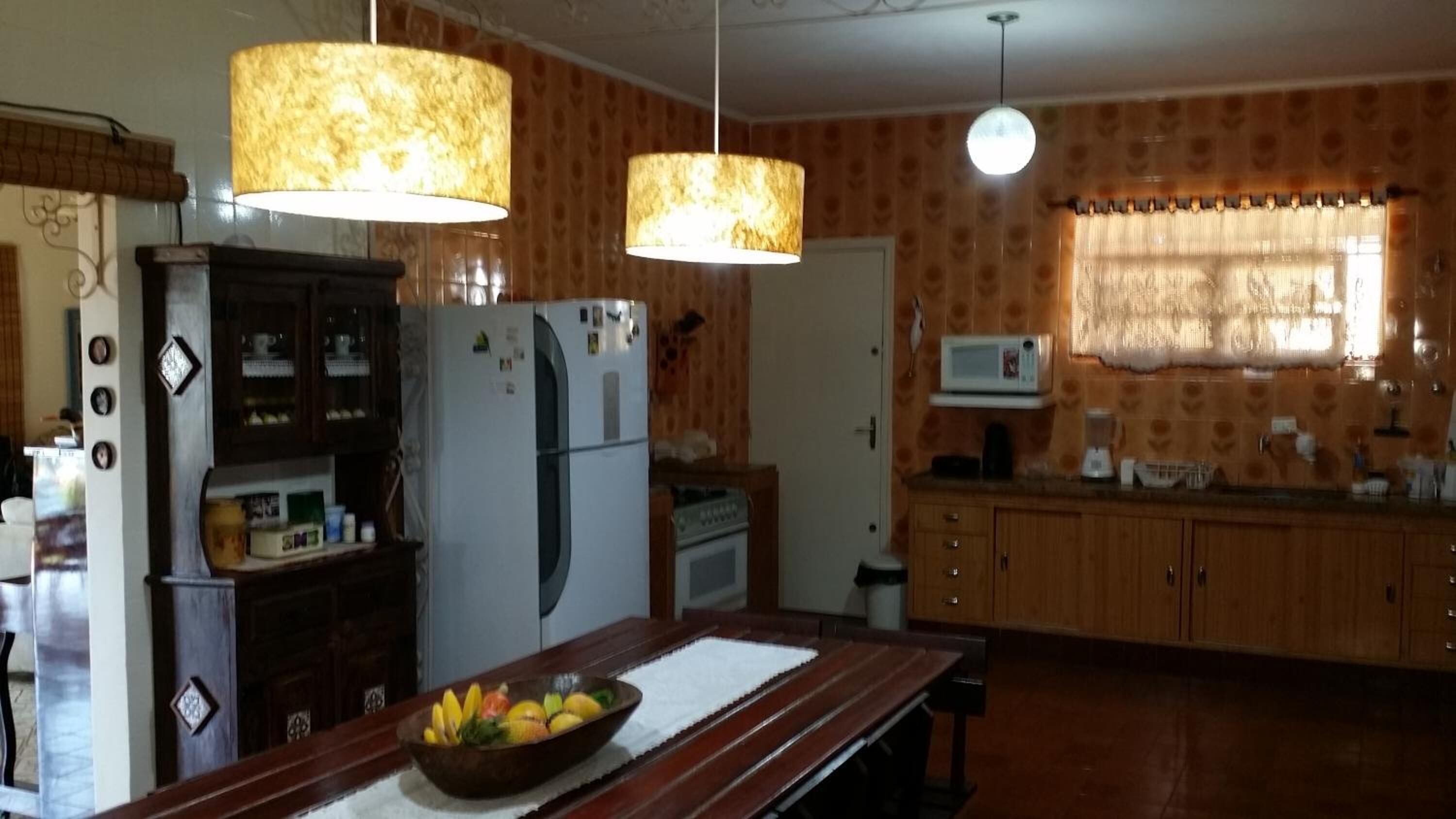 A kitchen with wooden cabinets, a refrigerator, a microwave, and a fruit bowl on the counter.