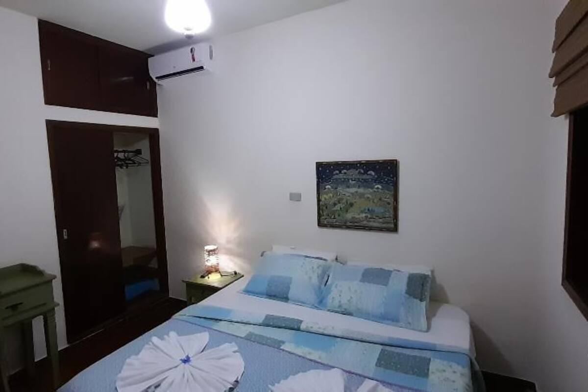 Un dormitorio con cama, cómoda, mesita de noche, aire acondicionado instalado en la pared, una puerta y una ventana.