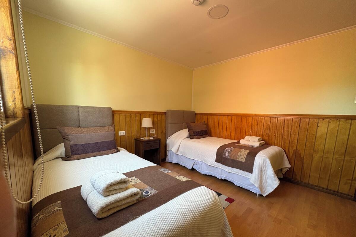 Een hotelkamer met twee bedden, houten lambrisering aan de wanden, een nachtkastje met een lamp en een kleine tafel.