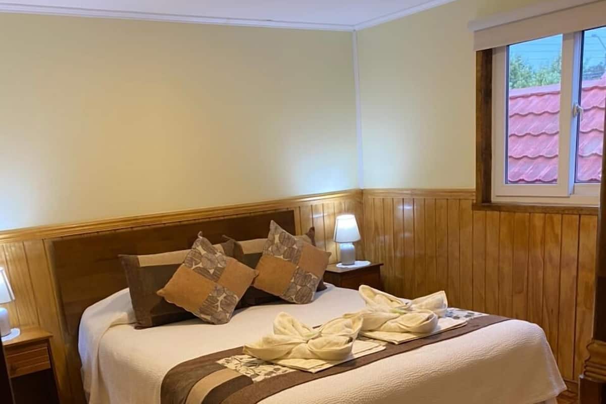 Een opgemaakt bed met een wit en bruin dekbed, twee kussens en een bedlampje.