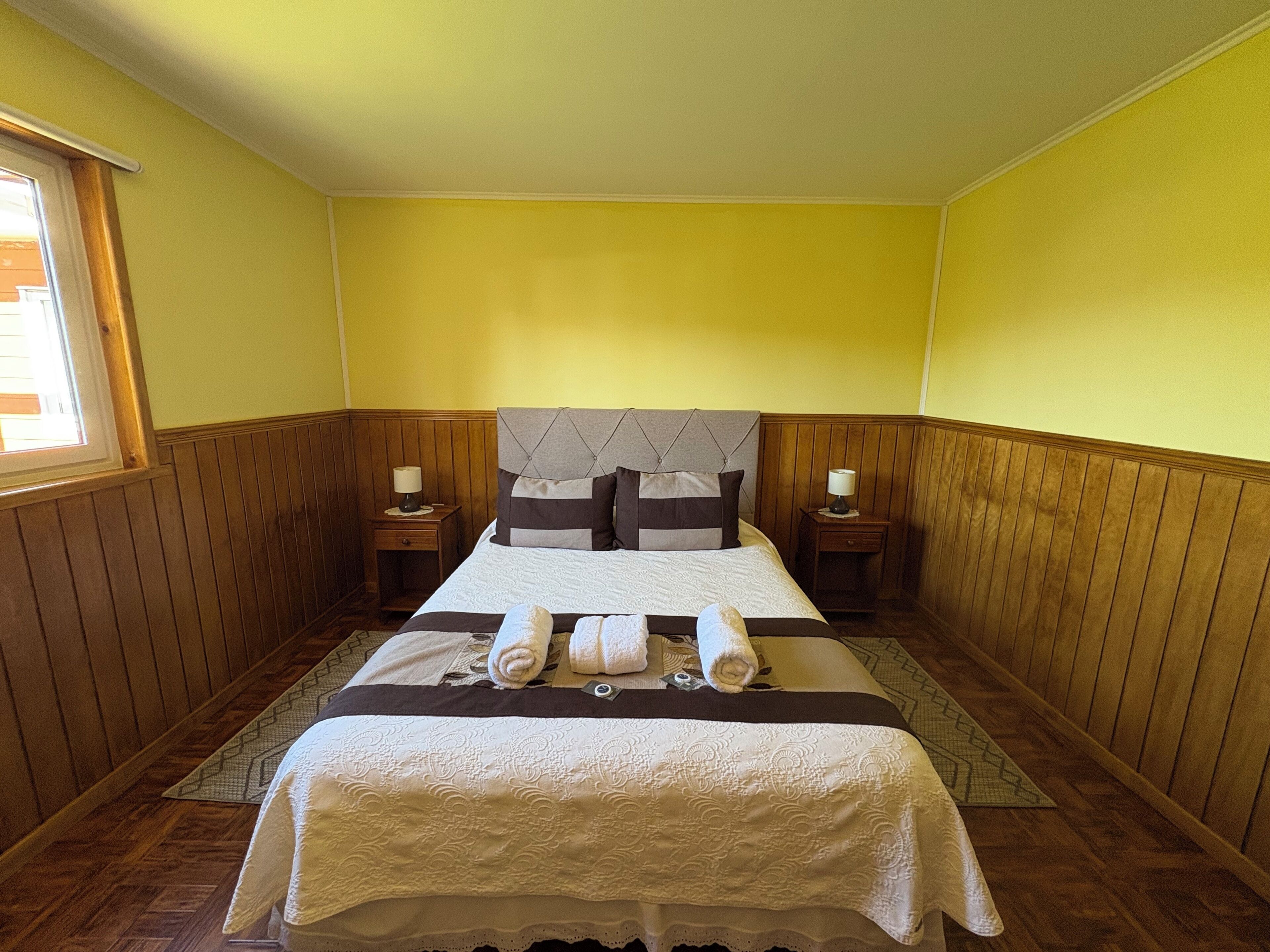 Un dormitorio con cama, dos mesitas de noche y ventana.