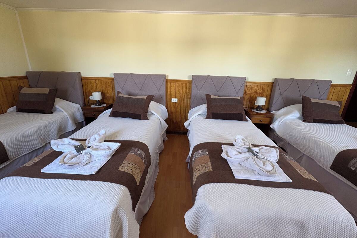 Een hotelkamer met vier eenpersoonsbedden, elk met hoofdeinde, nachtkastje en lamp.