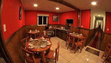 Un comedor con mesas y sillas de madera, una cocina al fondo y una pared roja.