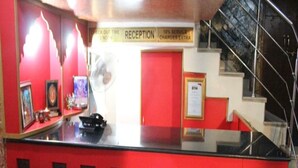 Un mostrador de recepción con una decoración en rojo y negro, un cartel que indica zona de recepción y una escalera al fondo.