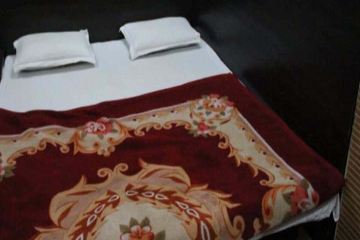A single bed with white linens and a red floral bedspread in a room with black walls and wooden blinds.