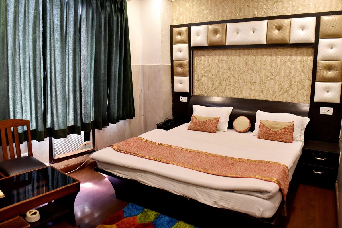 A hotel room with a large bed, a bedside table, a chair, a heater, and a window with curtains.