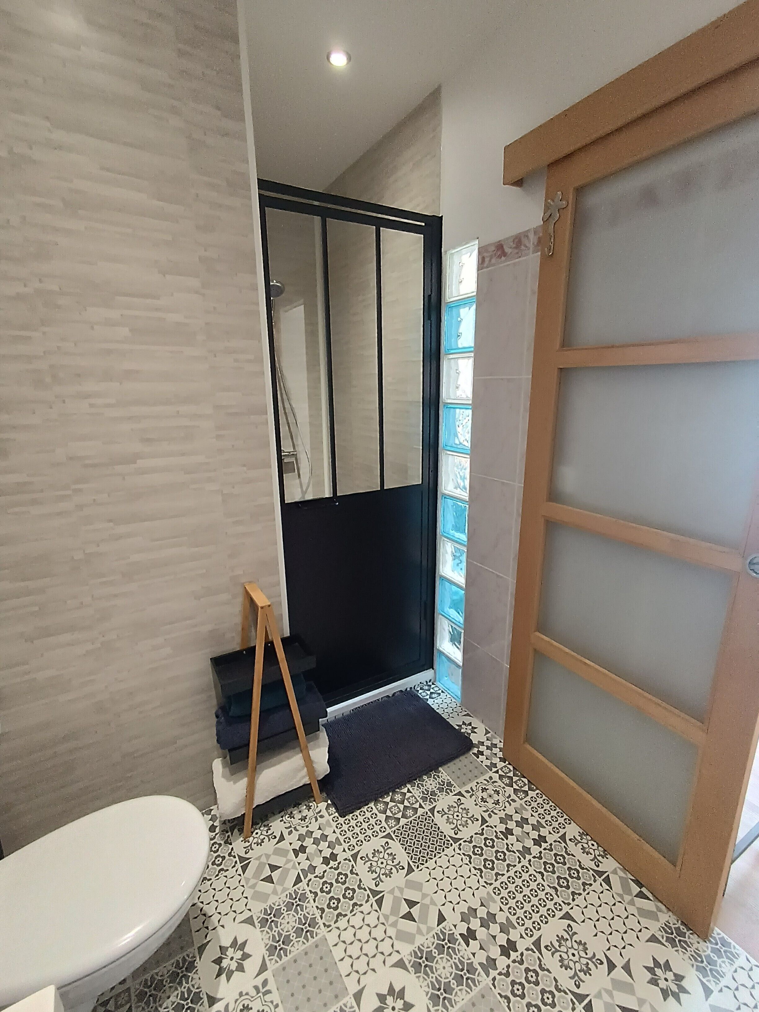 Un baño con inodoro, ducha de mampara de vidrio y suelo estampado.