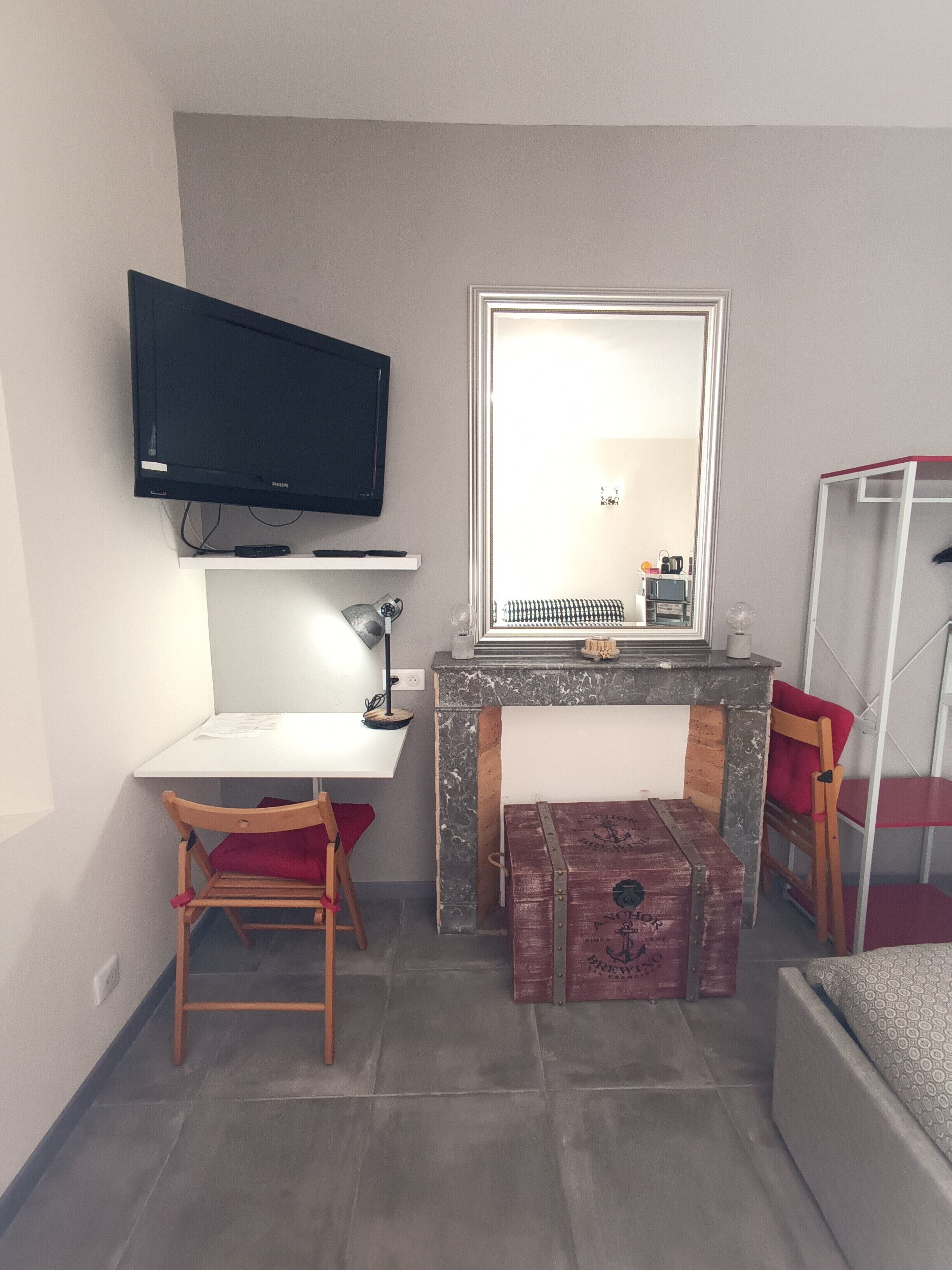 Une petite pièce comprenant un bureau, une chaise, une télévision, un miroir et un lit.