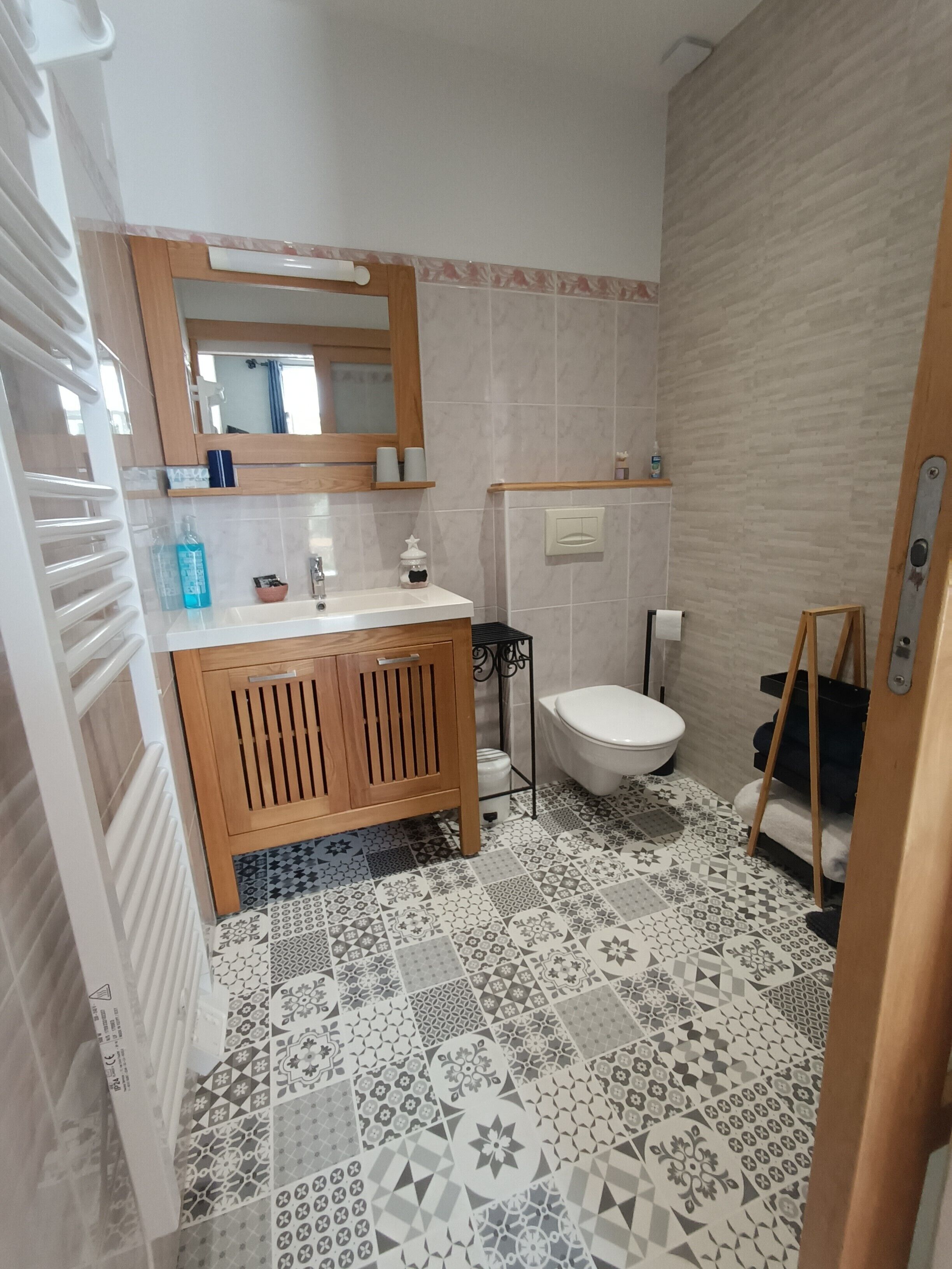 Un baño con tocador de madera, lavamanos, espejo, inodoro y baldosas de suelo estampadas.