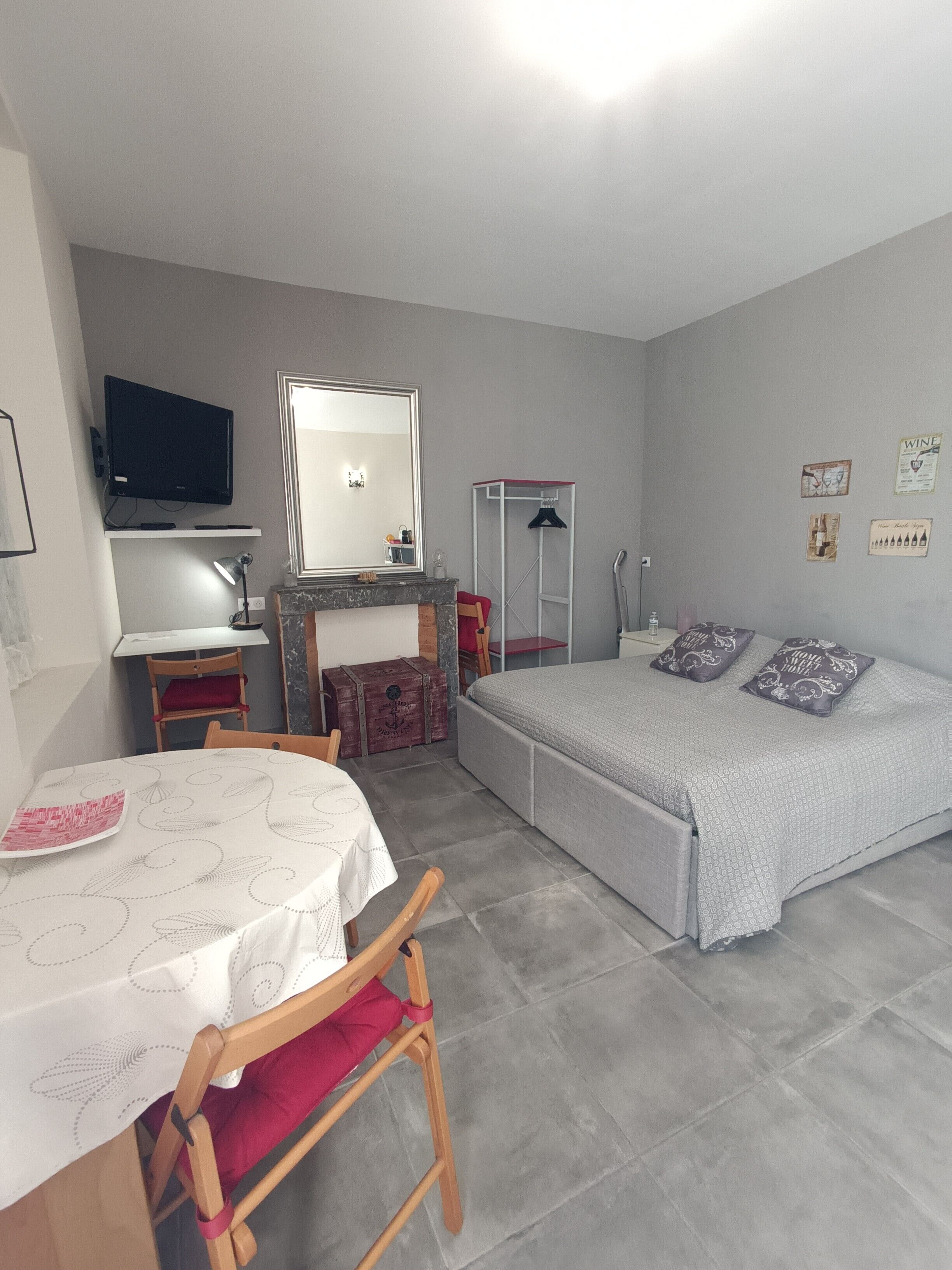 Un dormitorio con cama, escritorio con silla, televisión, espejo y armario.