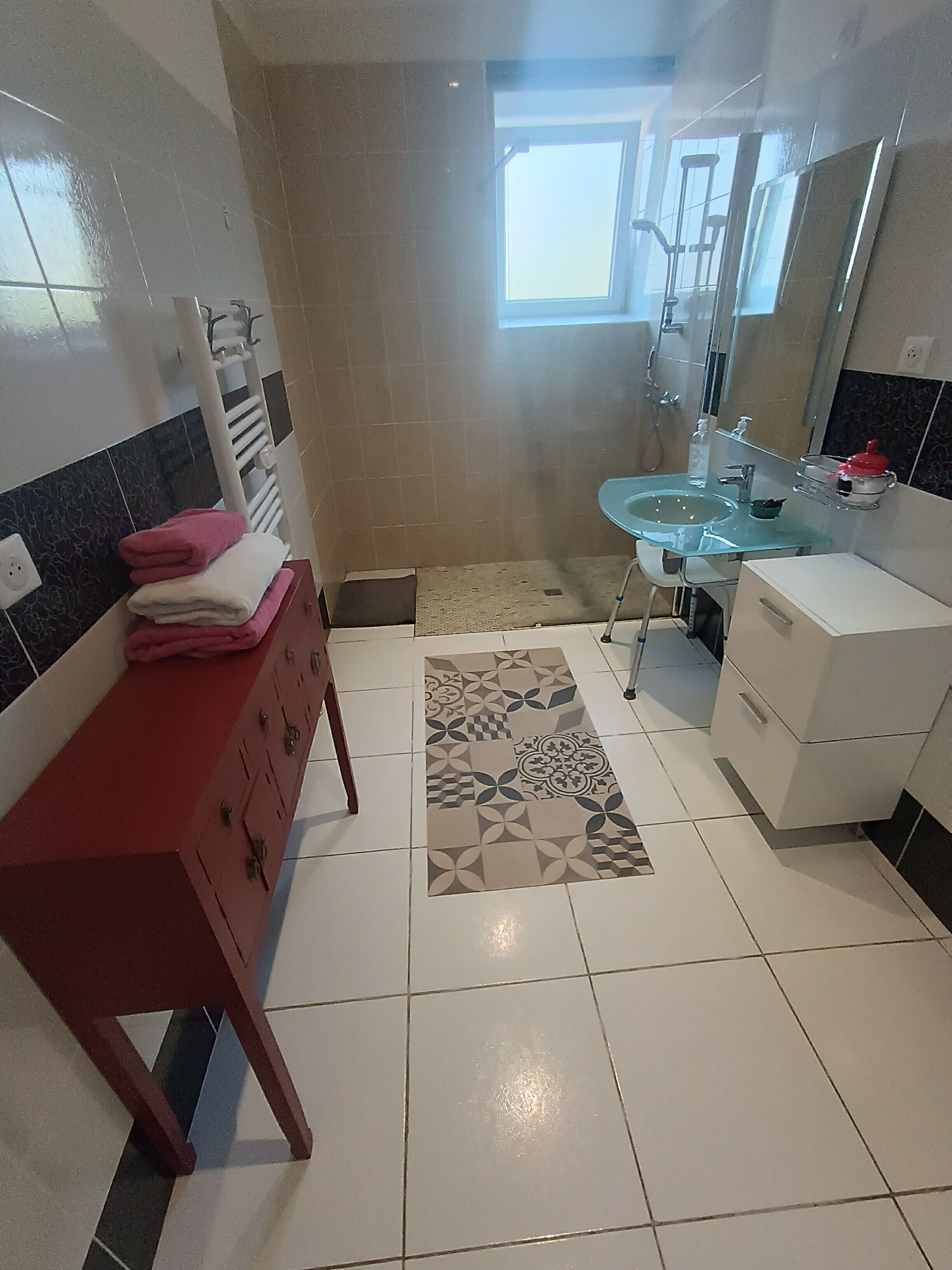 Un baño con tocador rojo, lavabo de vidrio y zona de ducha.