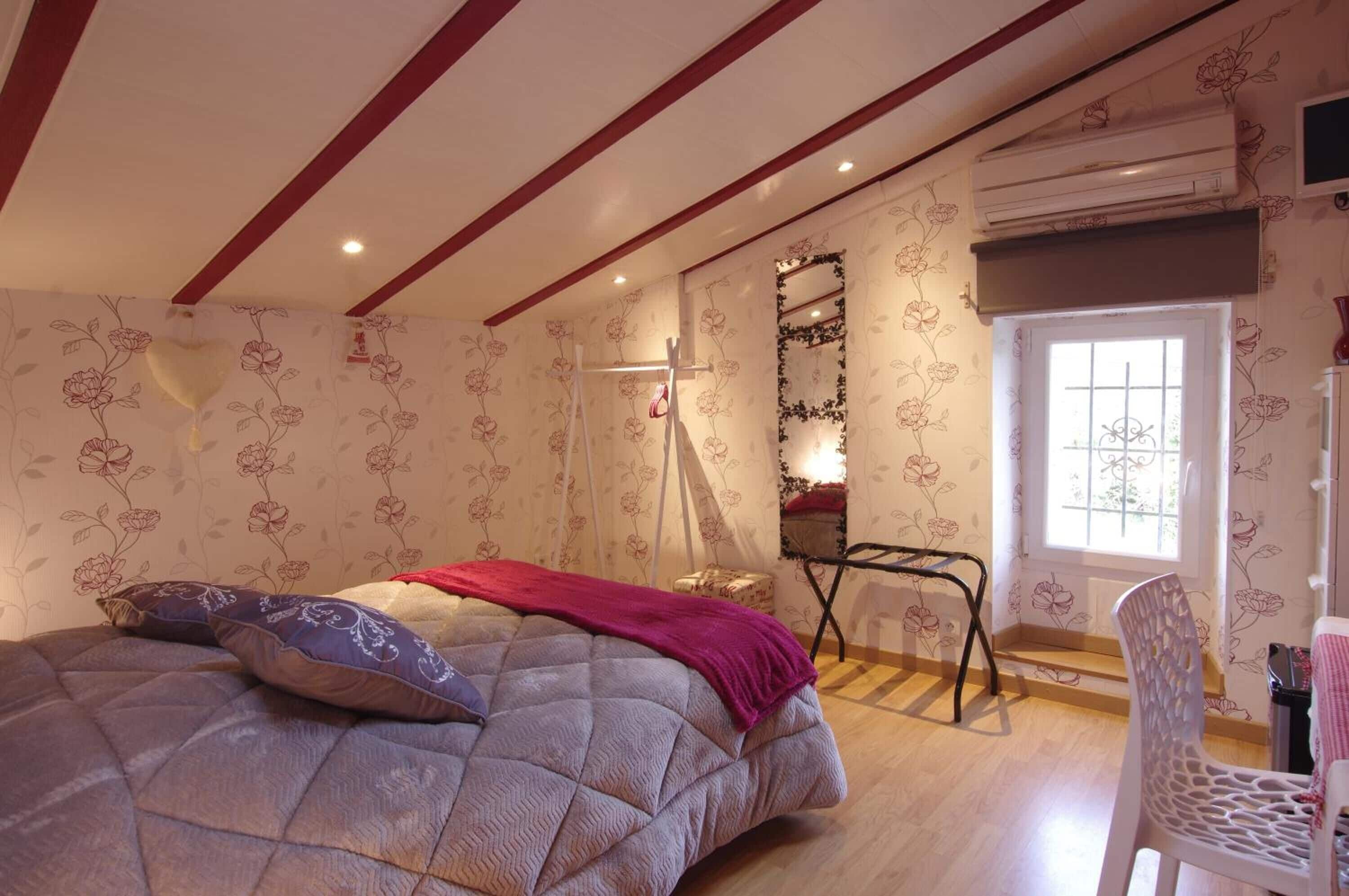 A bedroom with a bed, a chair, a mirror, and a window.
