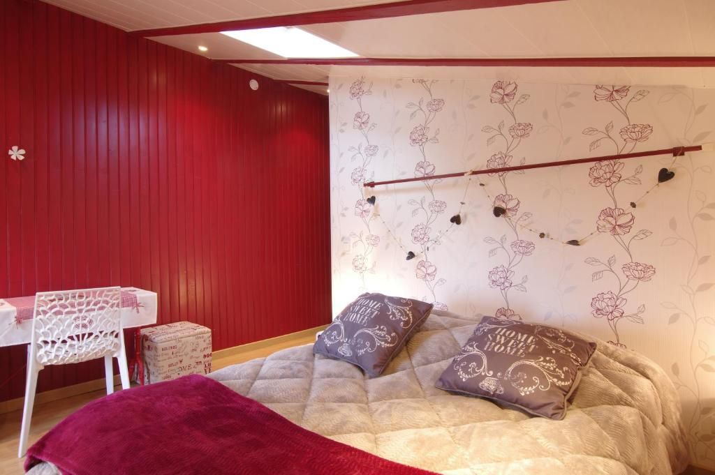 A bedroom with a bed, a red wall, a floral wallpaper, and a small table with a chair.