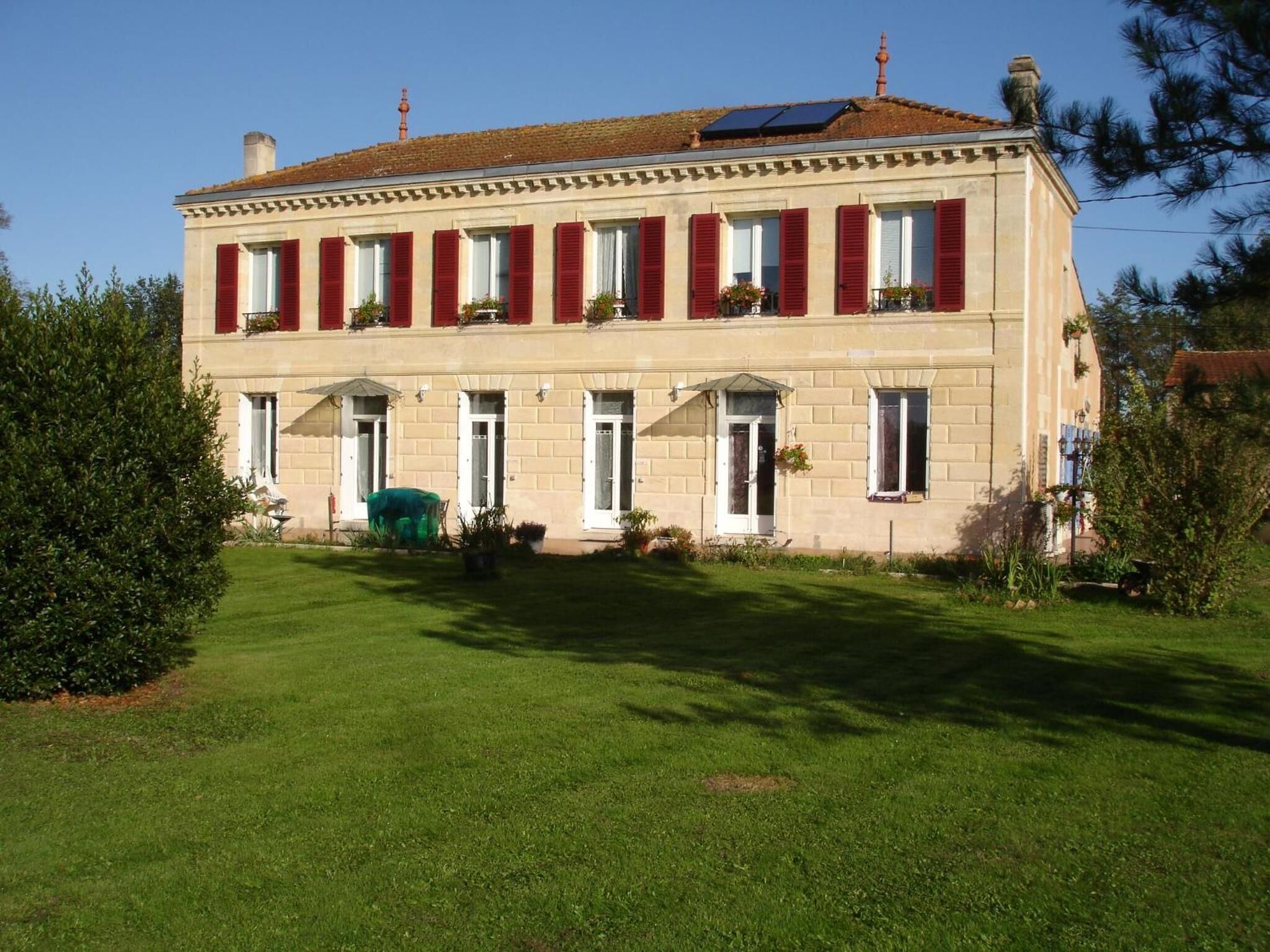 A two-story building with a symmetrical facade, red shutters, and a green lawn in front.