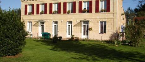 A two-story building with a symmetrical facade, red shutters, and a green lawn in front.