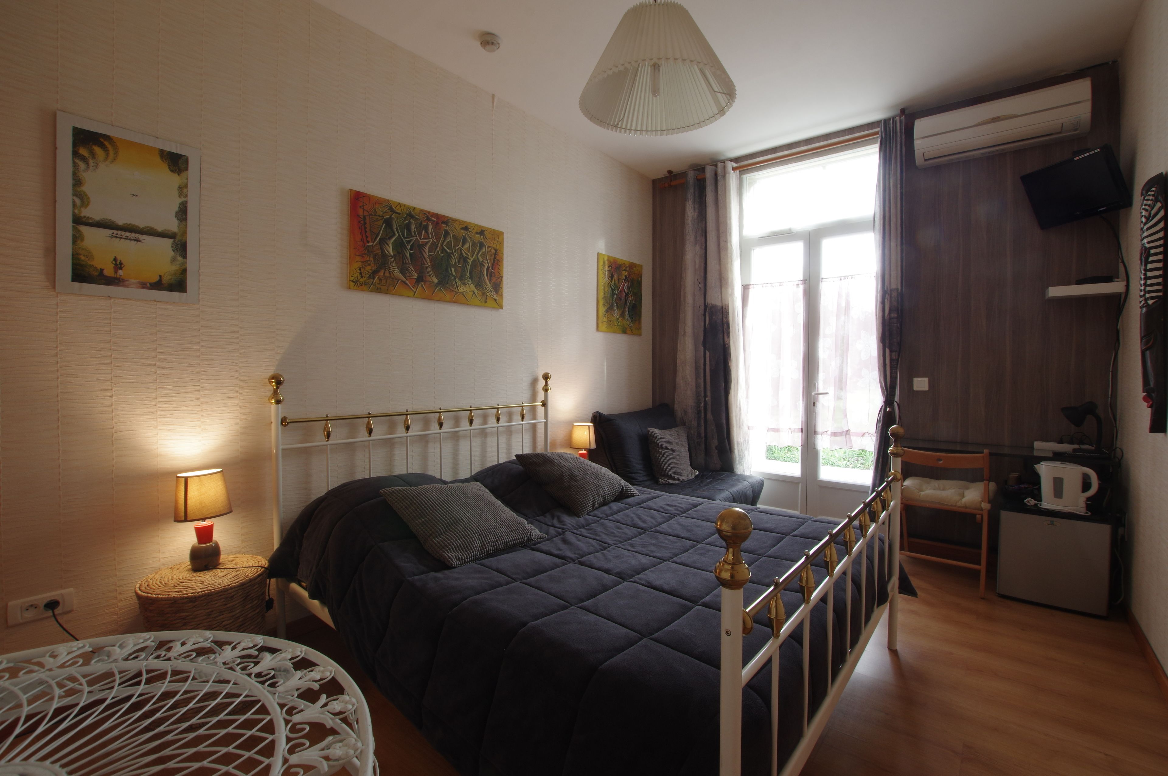Un dormitorio con cama, lámparas de noche, una mesita, una silla, televisor y ventana con cortinas.