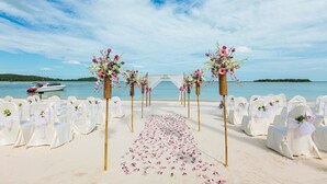 Une cérémonie de mariage organisée sur la plage, avec des chaises blanches et des décorations florales.