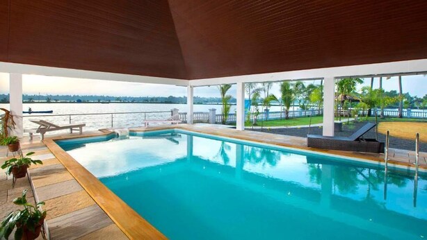 Une piscine intérieure donnant sur le plan d’eau extérieur, entourée de plantes en pot et de chaises longues.
