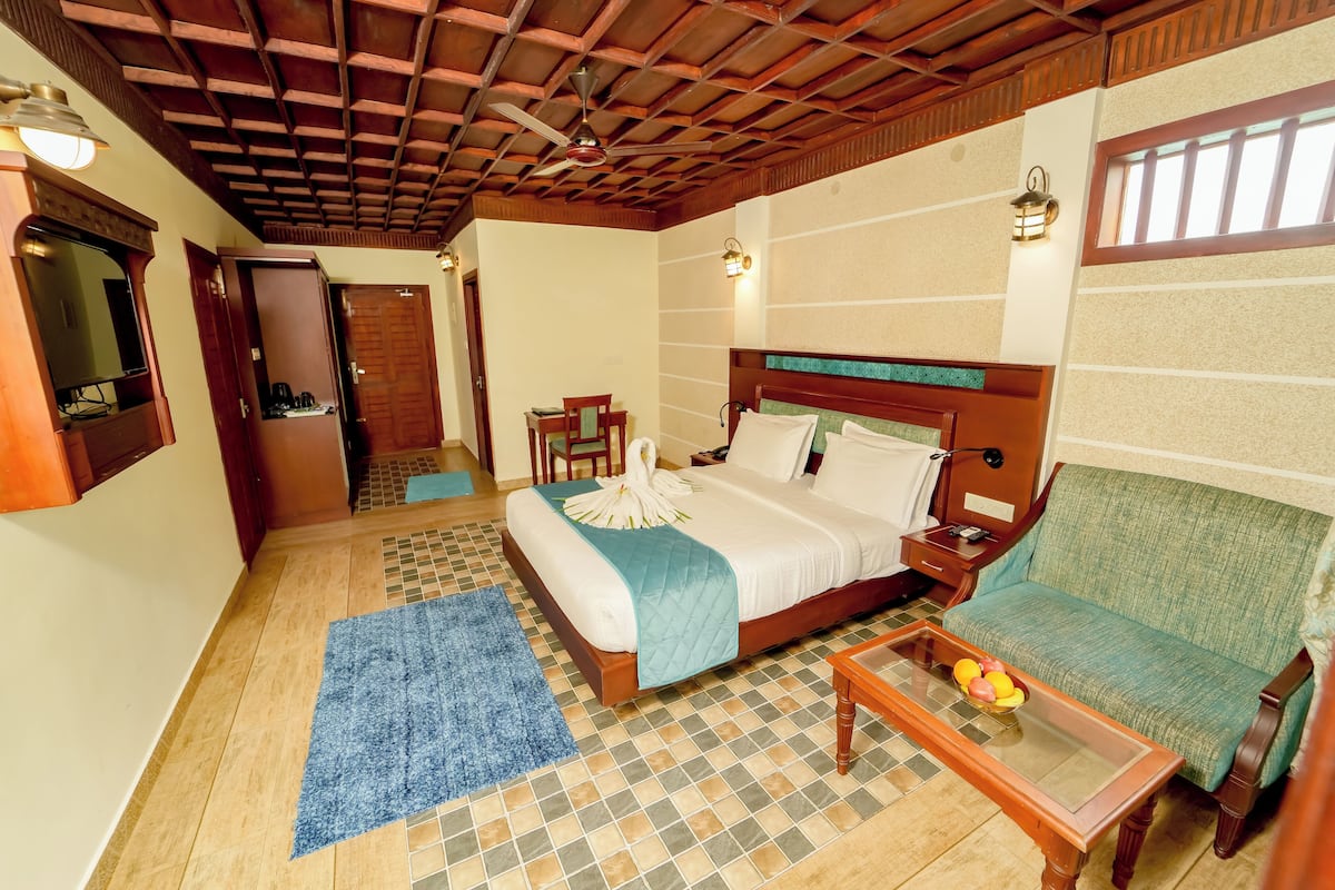 A hotel room with a bed, a sofa, a coffee table, a blue rug, and a wooden ceiling.