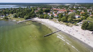 Vue aérienne d’une ville côtière avec une plage de sable, une jetée et des immeubles résidentiels.