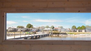 Une vue à travers une fenêtre d’une propriété située au bord de l’eau, avec une terrasse en bois, un quai et plusieurs petites maisons.