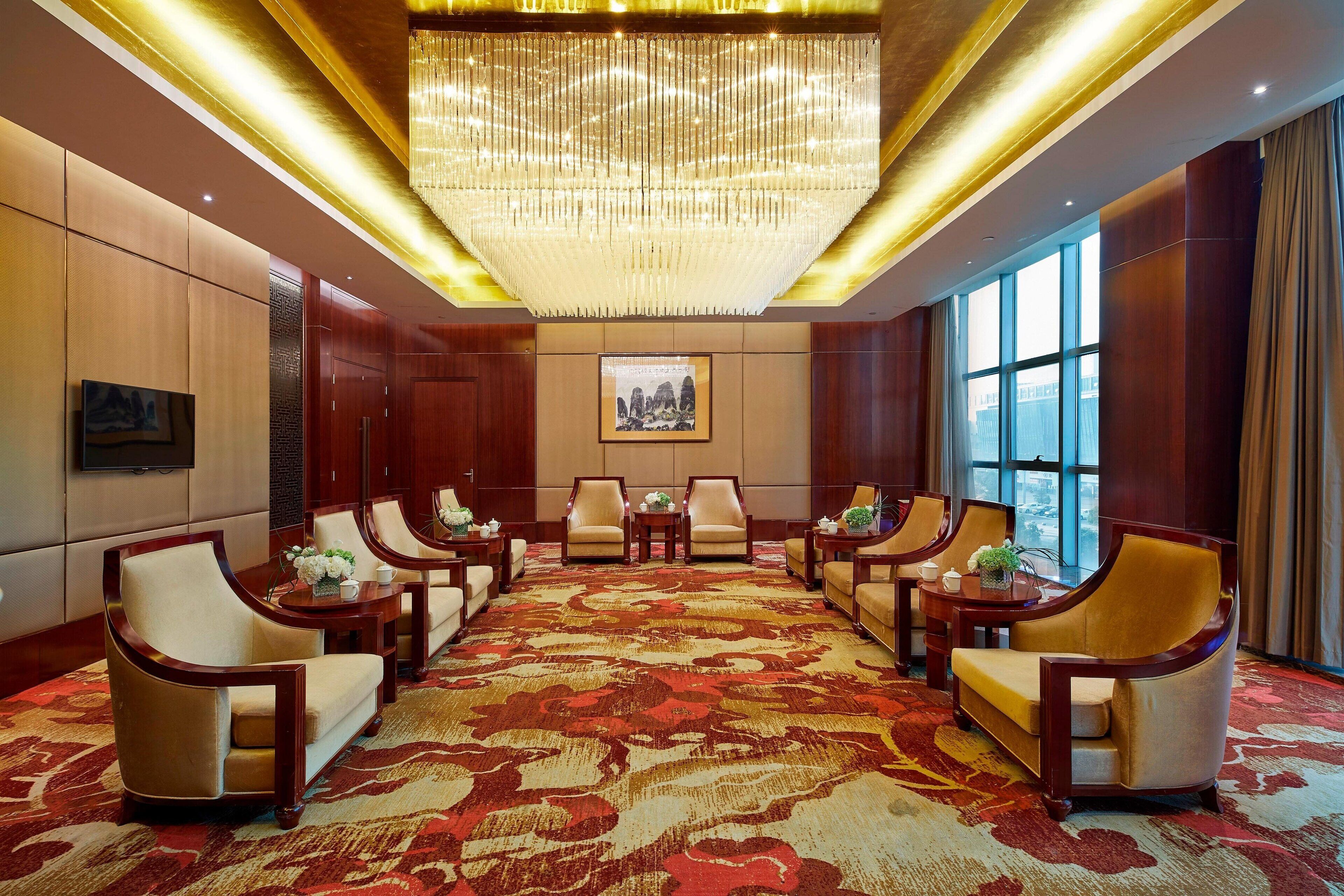 A spacious conference room with a large chandelier, wooden paneling, and a patterned carpet.