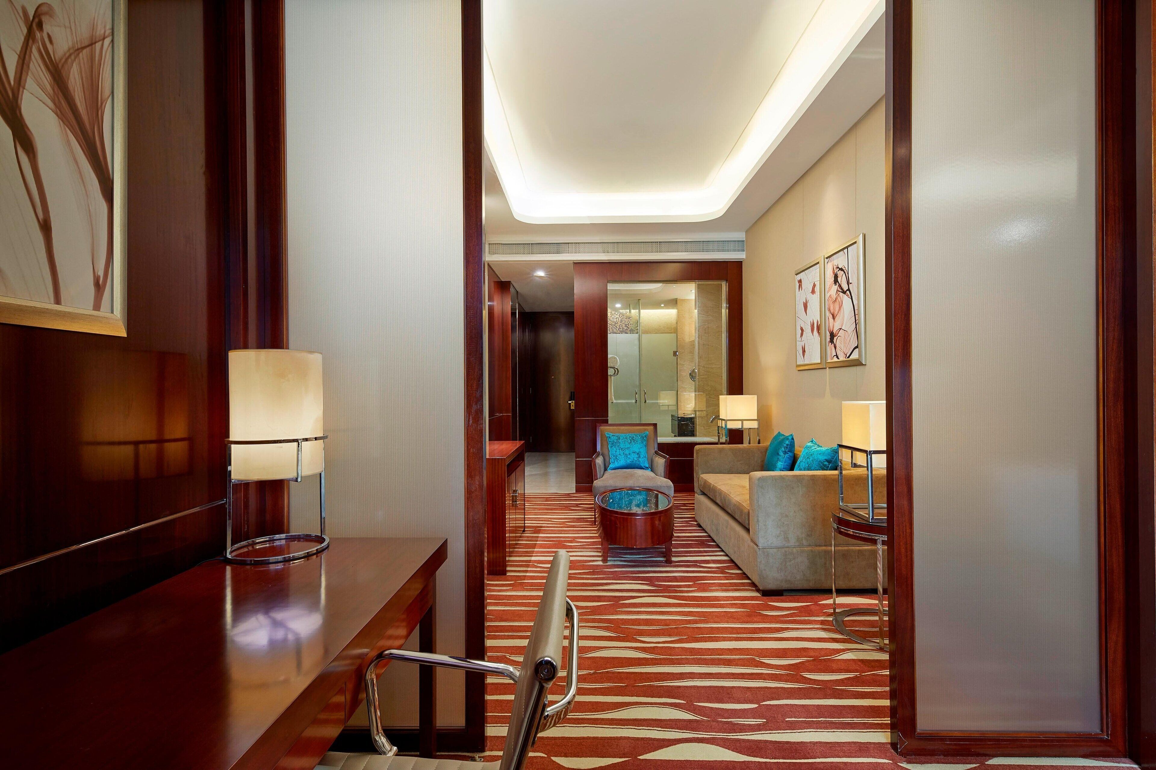 A hotel lobby with a wooden reception desk, a glass coffee table, a sofa, and a patterned carpet.