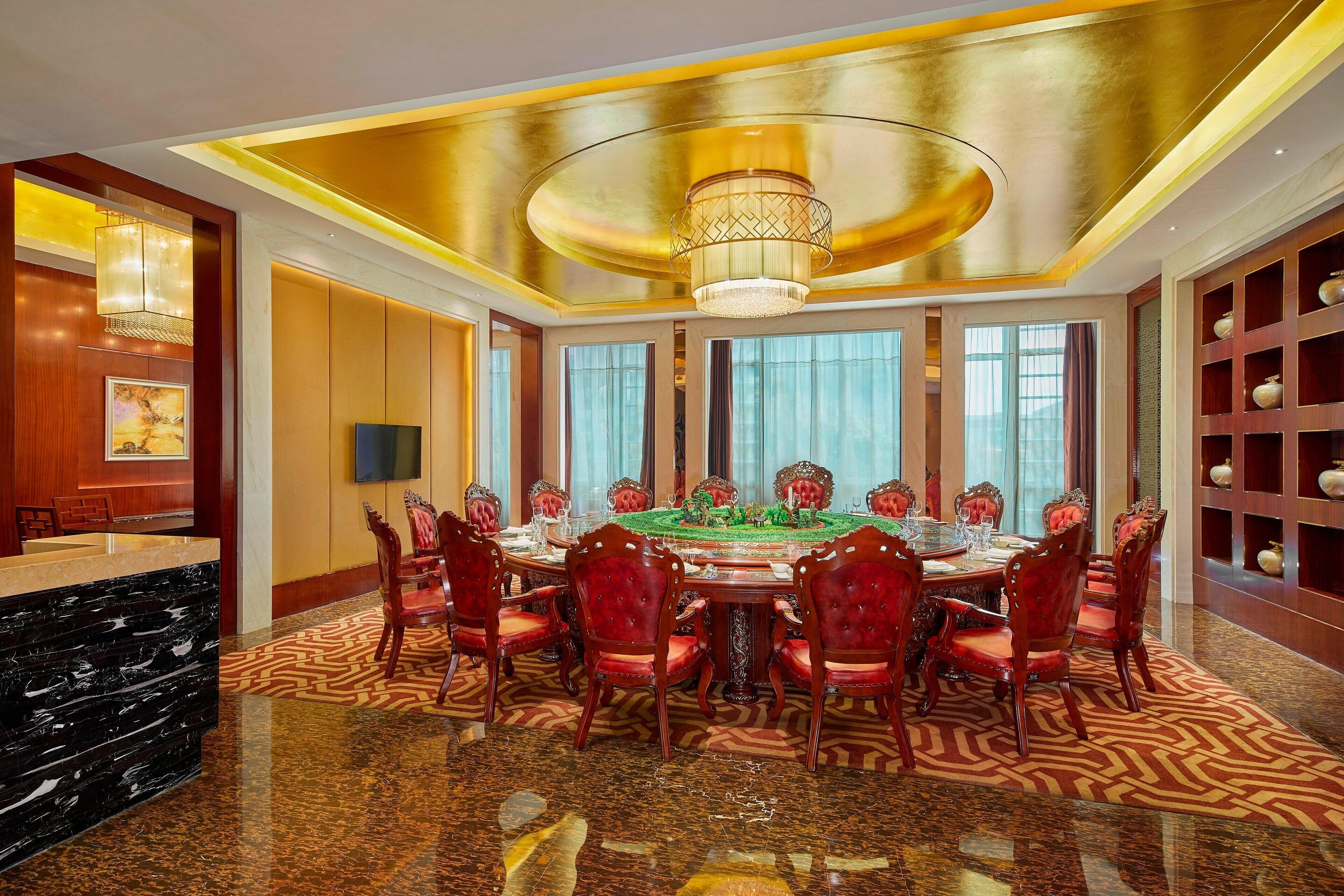 A luxurious dining room with a round table, red upholstered chairs, and a chandelier.