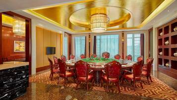 A luxurious dining room with a round table, red upholstered chairs, and a chandelier.