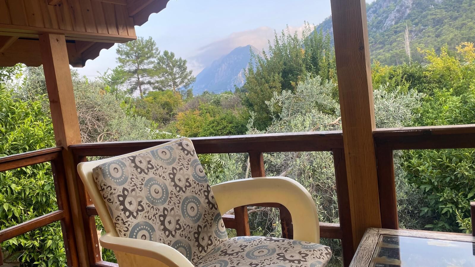 Um terraço de madeira com uma cadeira e mesa, com vista para uma paisagem montanhosa.