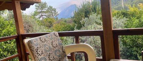 Um terraço de madeira com uma cadeira e mesa, com vista para uma paisagem montanhosa.