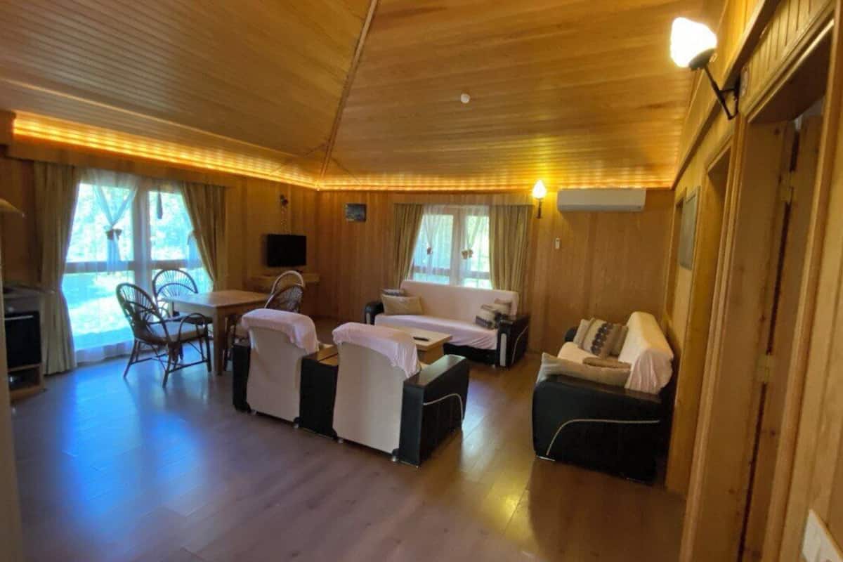 A wooden cabin interior with a dining area, a sofa, a bed, and a TV.