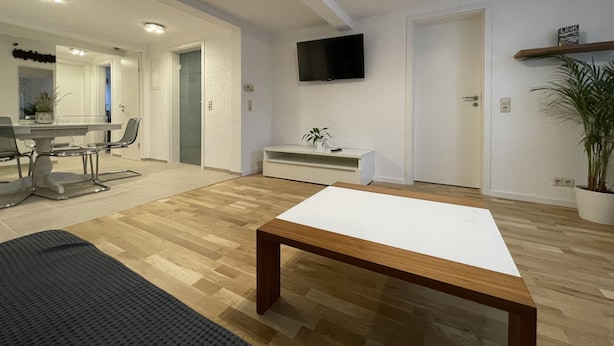 A modern living room with a wooden coffee table, a flat-screen TV mounted on the wall, and a dining area with a white table and chairs. - Fewo Reutlingen Metzstrasse (Reutlingen)