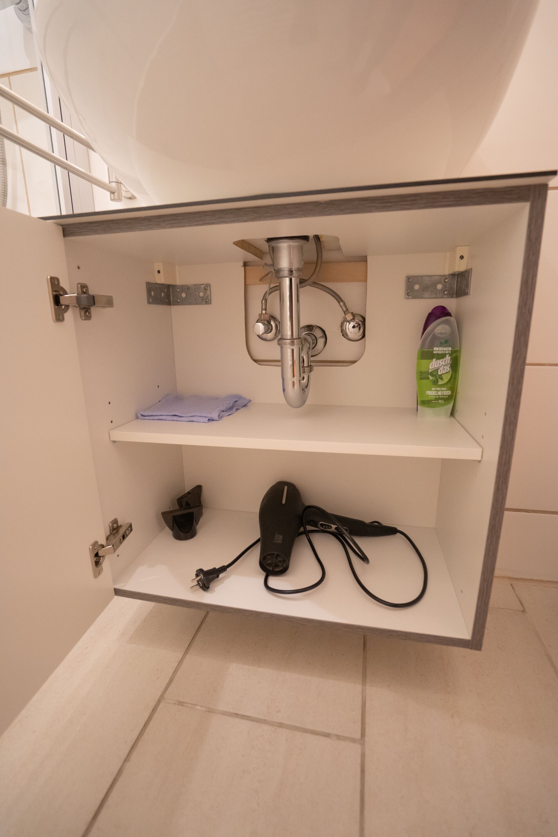A bathroom with a built-in sink, a towel rack, and a shelf with a bottle of cleaning product.